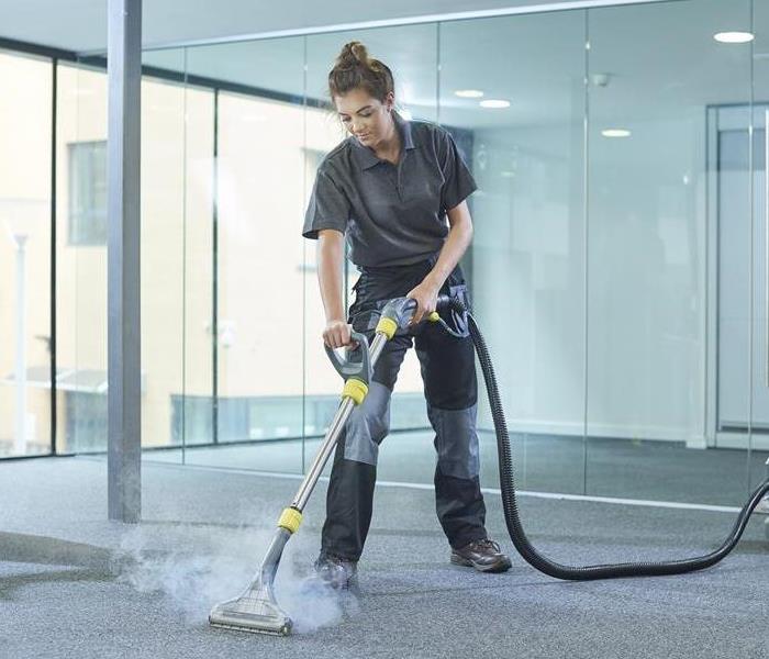 A female cleaning contractor steam cleans an office carpet in a empty office in between tenants